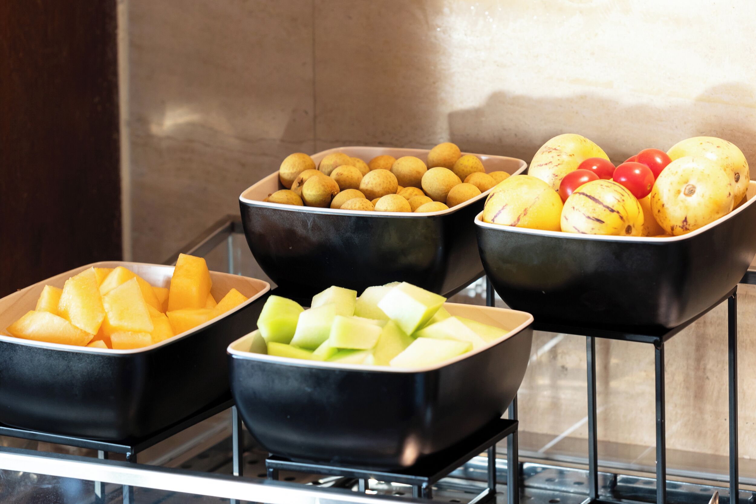 Three black bowls containing different fruits on a metal rack.