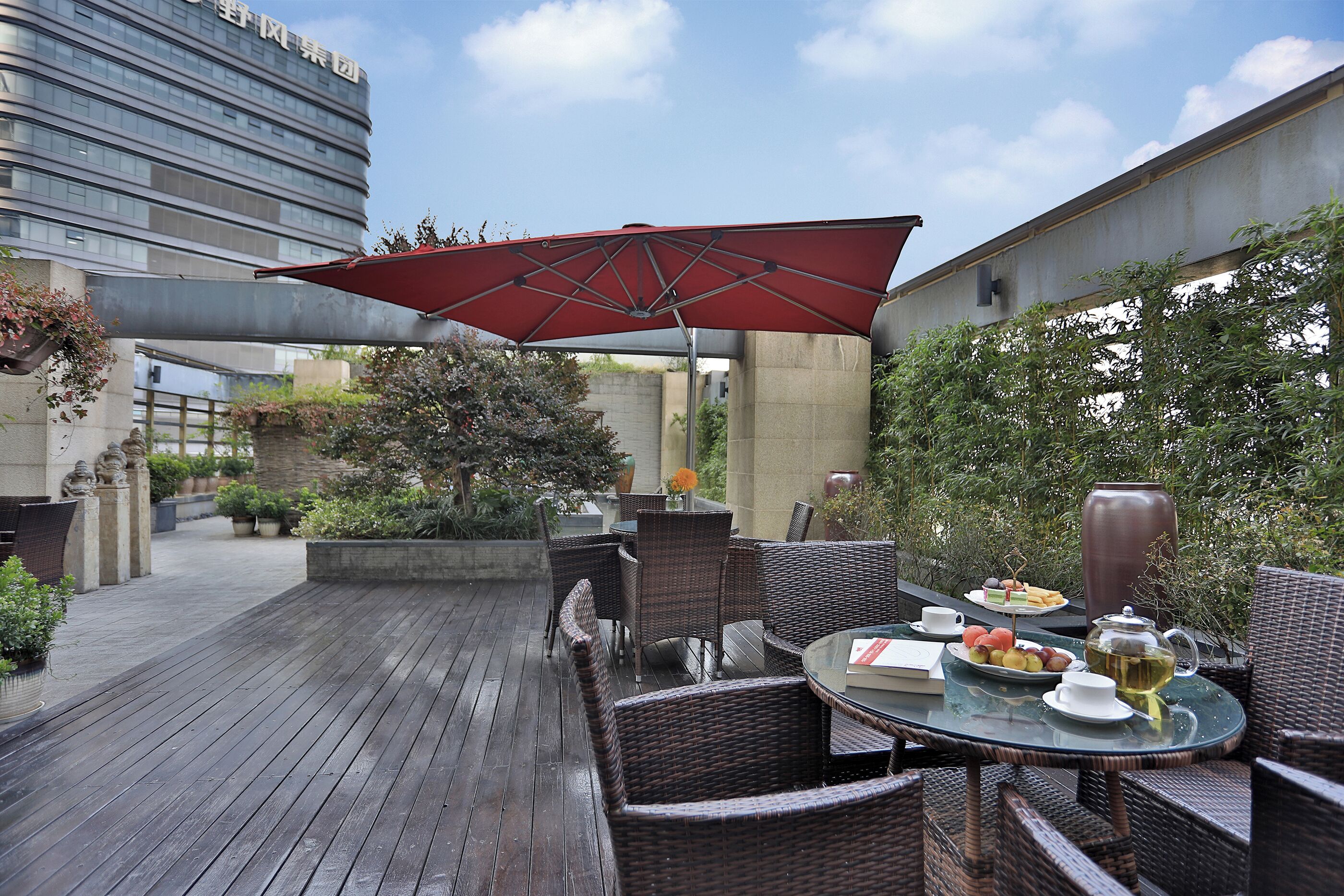 An outdoor patio with wicker furniture, a table set with a teapot, cups, and a plate of fruit.