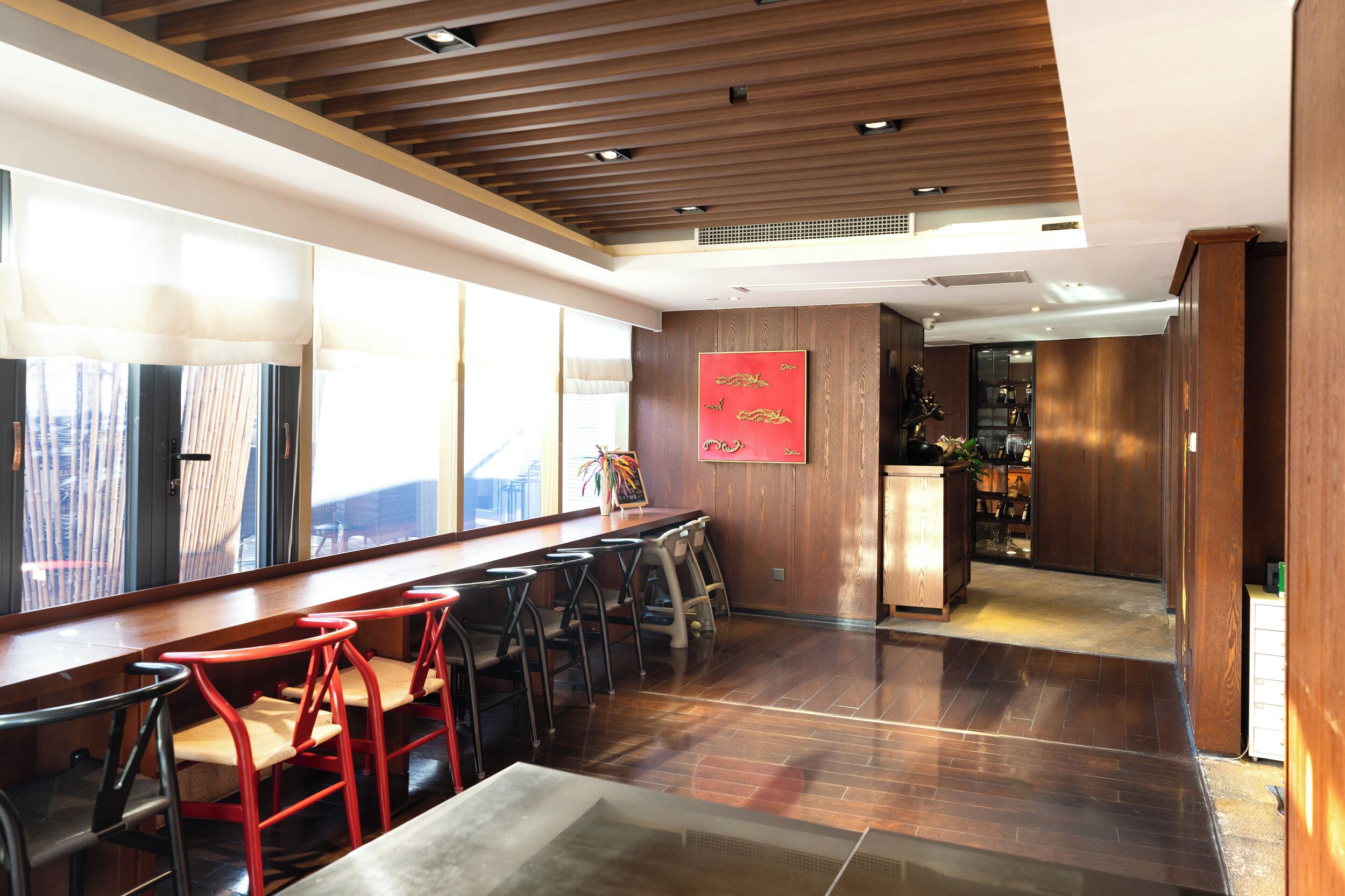 A restaurant with wooden floors, red bar stools, and a bar area.