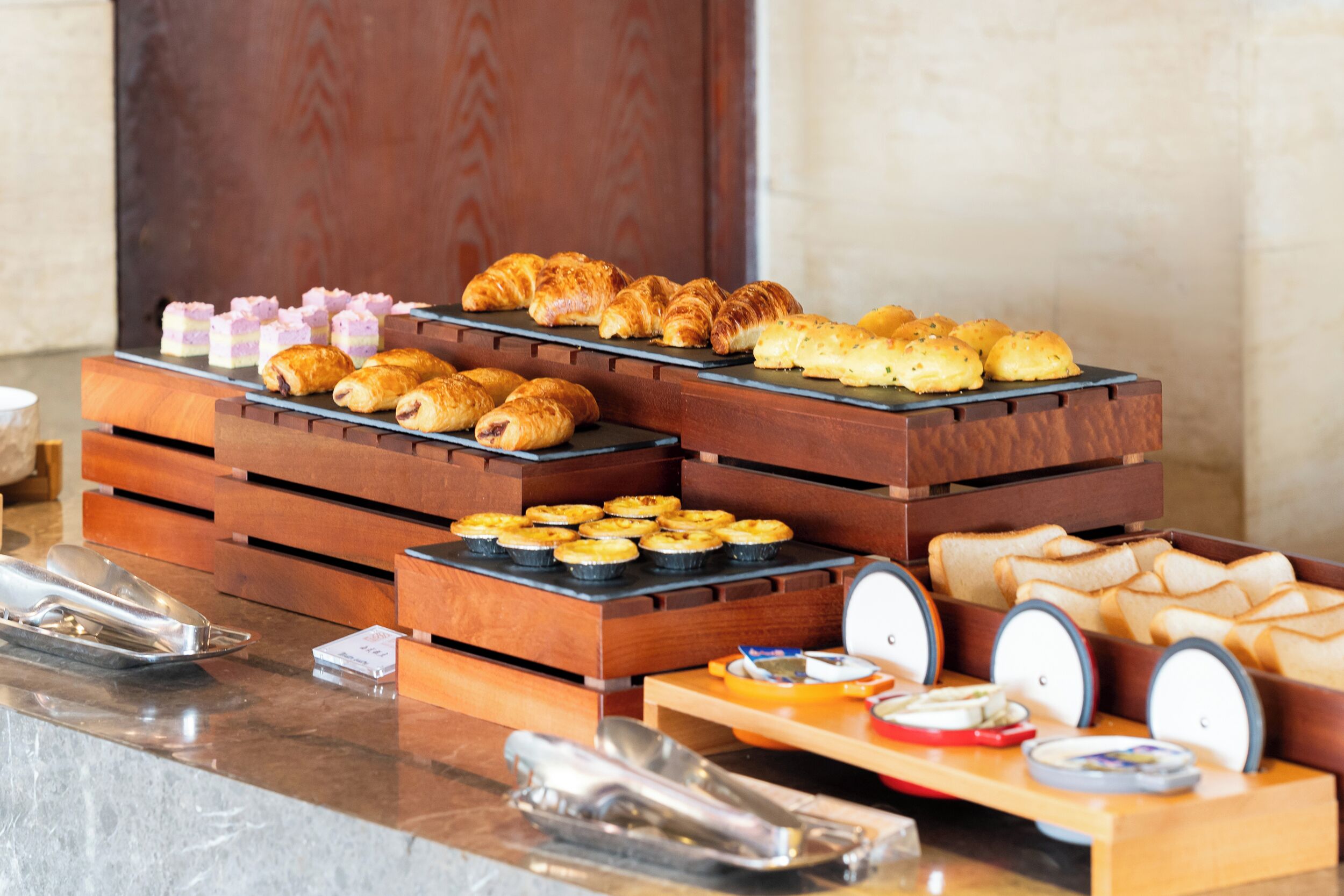 A buffet with various pastries and bread displayed on wooden stands.