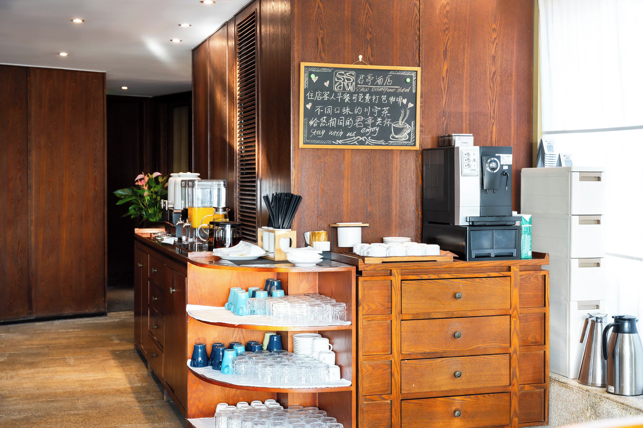 A hotel reception area with a wooden counter, a chalkboard sign, and various amenities like a coffee machine and a kettle.