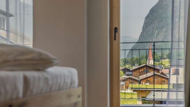 A bed with a wooden headboard and a window view of a mountain and a church. - Newly built chalet in the middle of the Ötztal (Umhausen)
