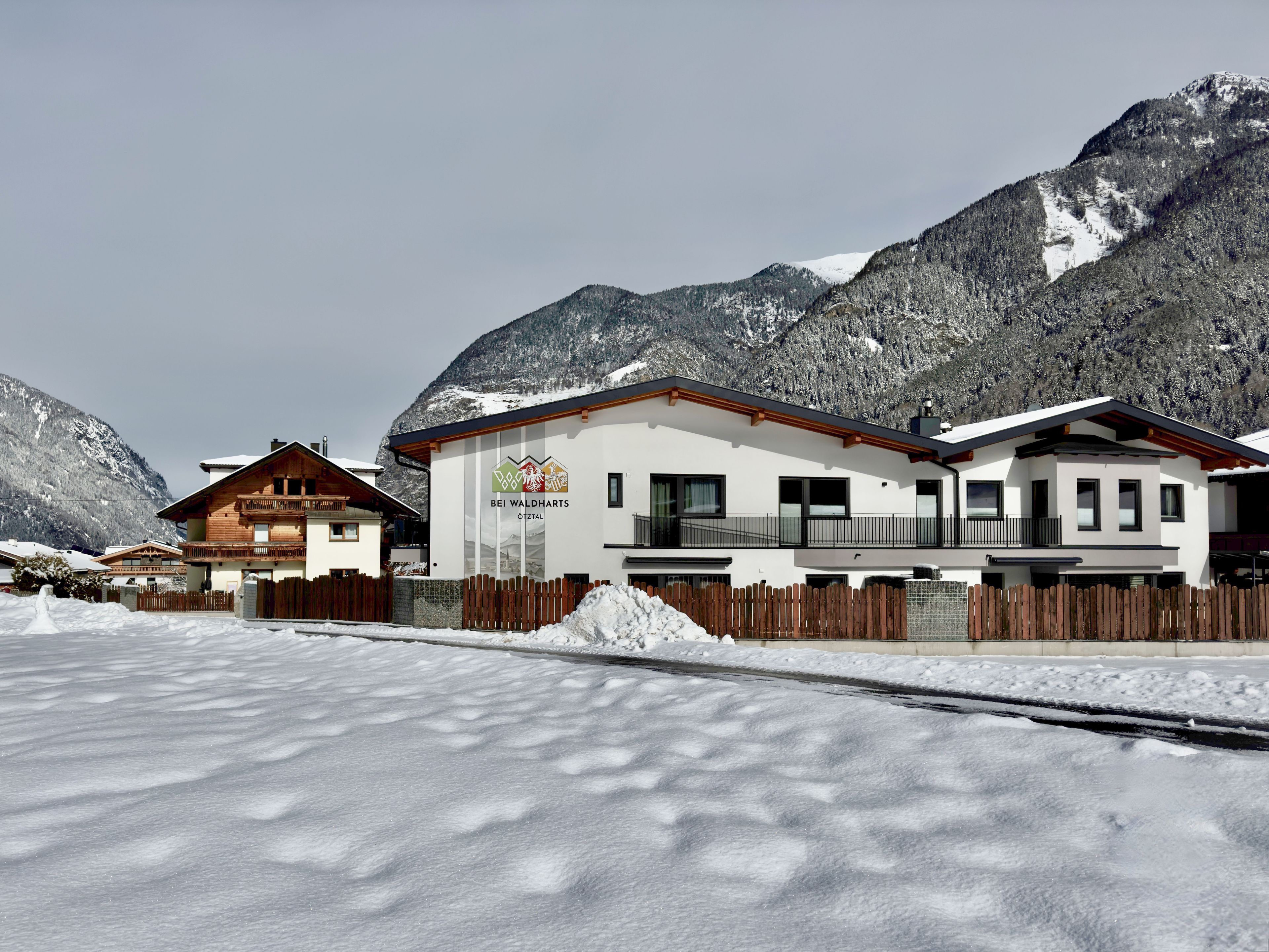 A hotel with a modern design, featuring a prominent logo on the facade, situated in a mountainous area with snow-covered surroundings.