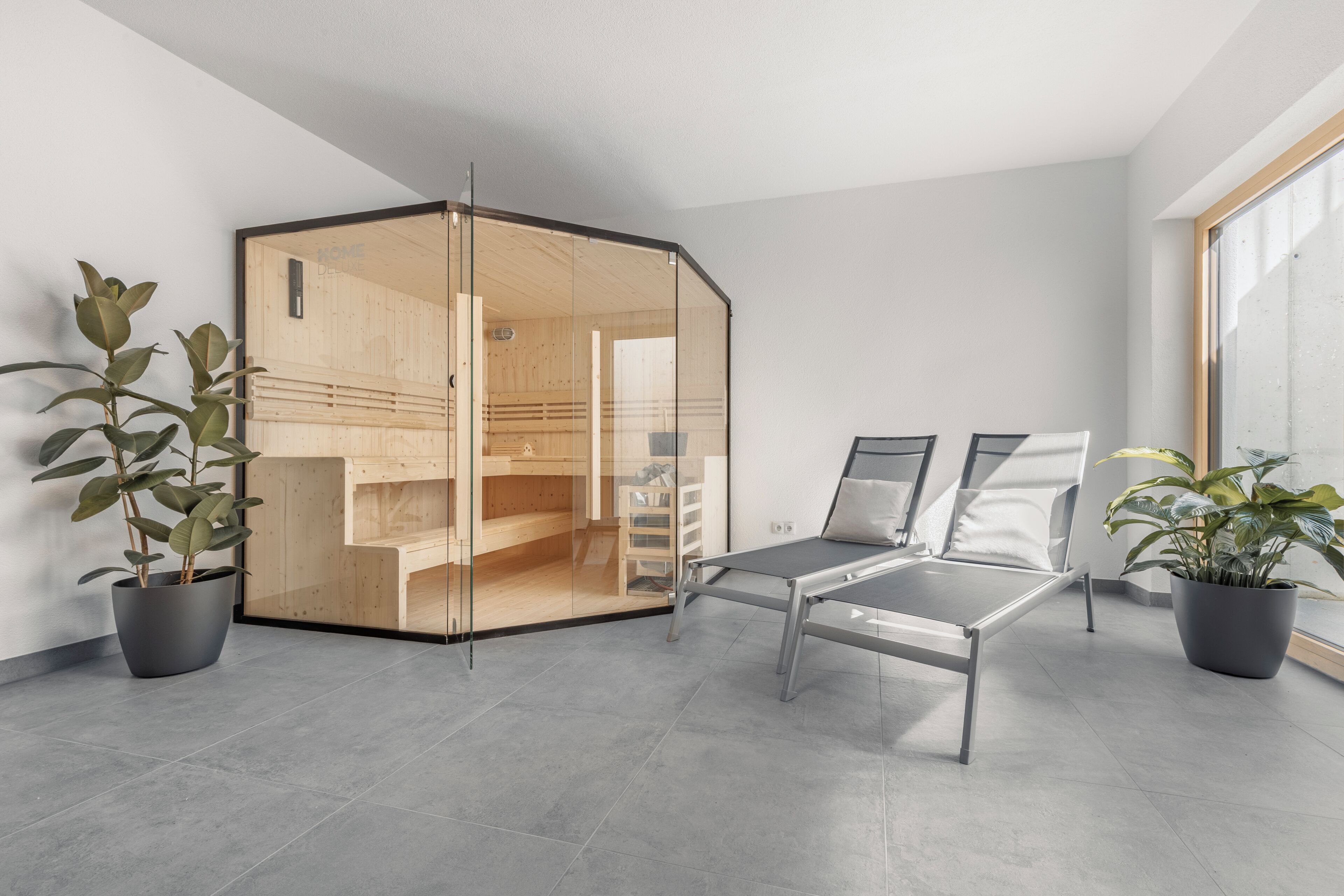 Een moderne hotelkamer met een glazen scheidingswand, een bed, een bureau en potplanten.
