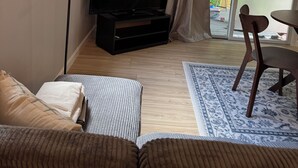 Ett vardagsrum med en soffa, en tv, en lampa och utsikt över utomhusmiljön genom en skjutdörr i glas.