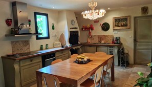 Een keuken met een houten tafel, stoelen, een kroonluchter en diverse keukenapparaten.