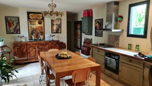 Une cuisine avec des meubles de rangement en bois, une table à manger avec des chaises, un lustre et divers appareils de cuisine.