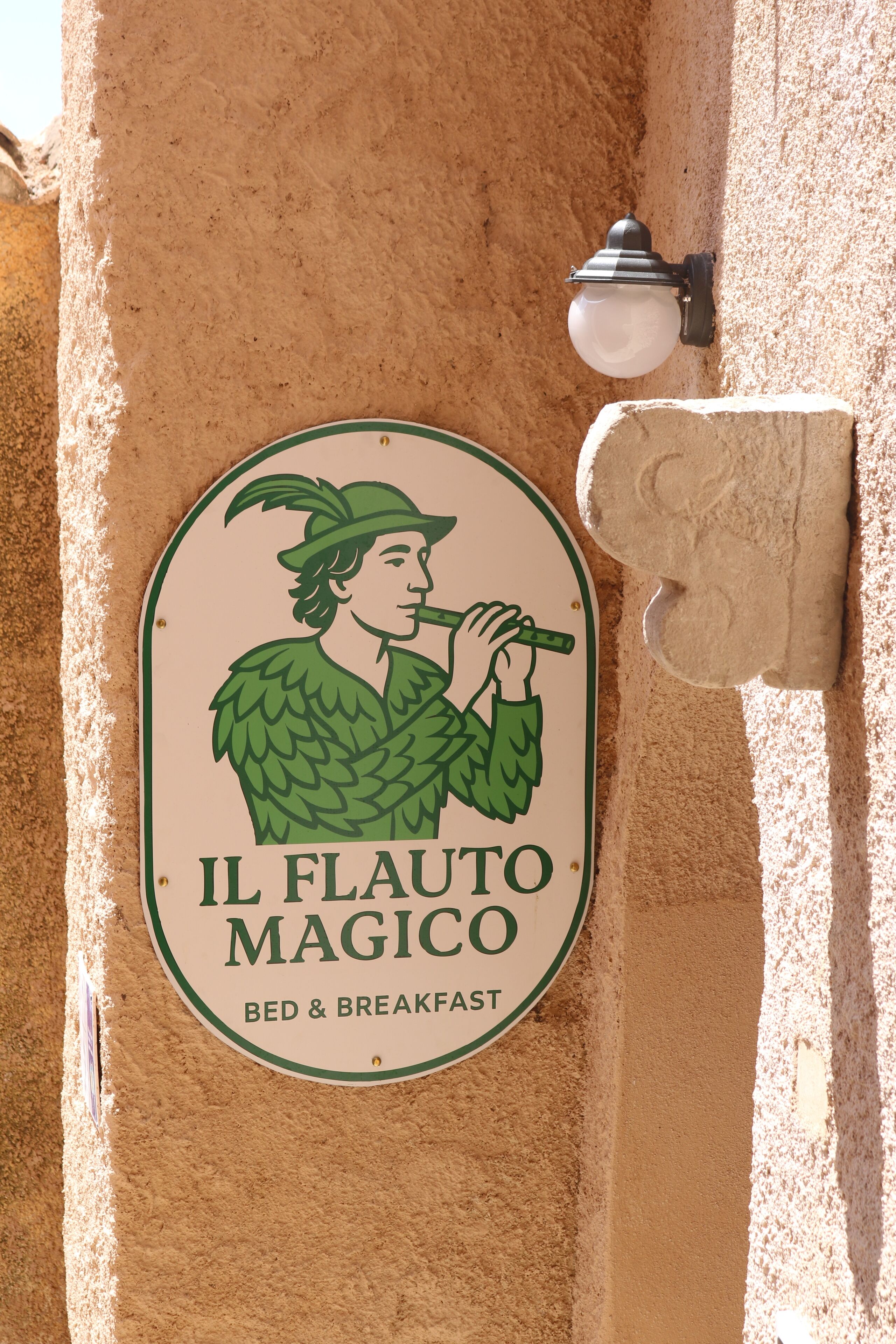 Schild für das Bed & Breakfast "Il Flauto Magico" mit einer Illustration eines gefiederten Wesens in Grün.