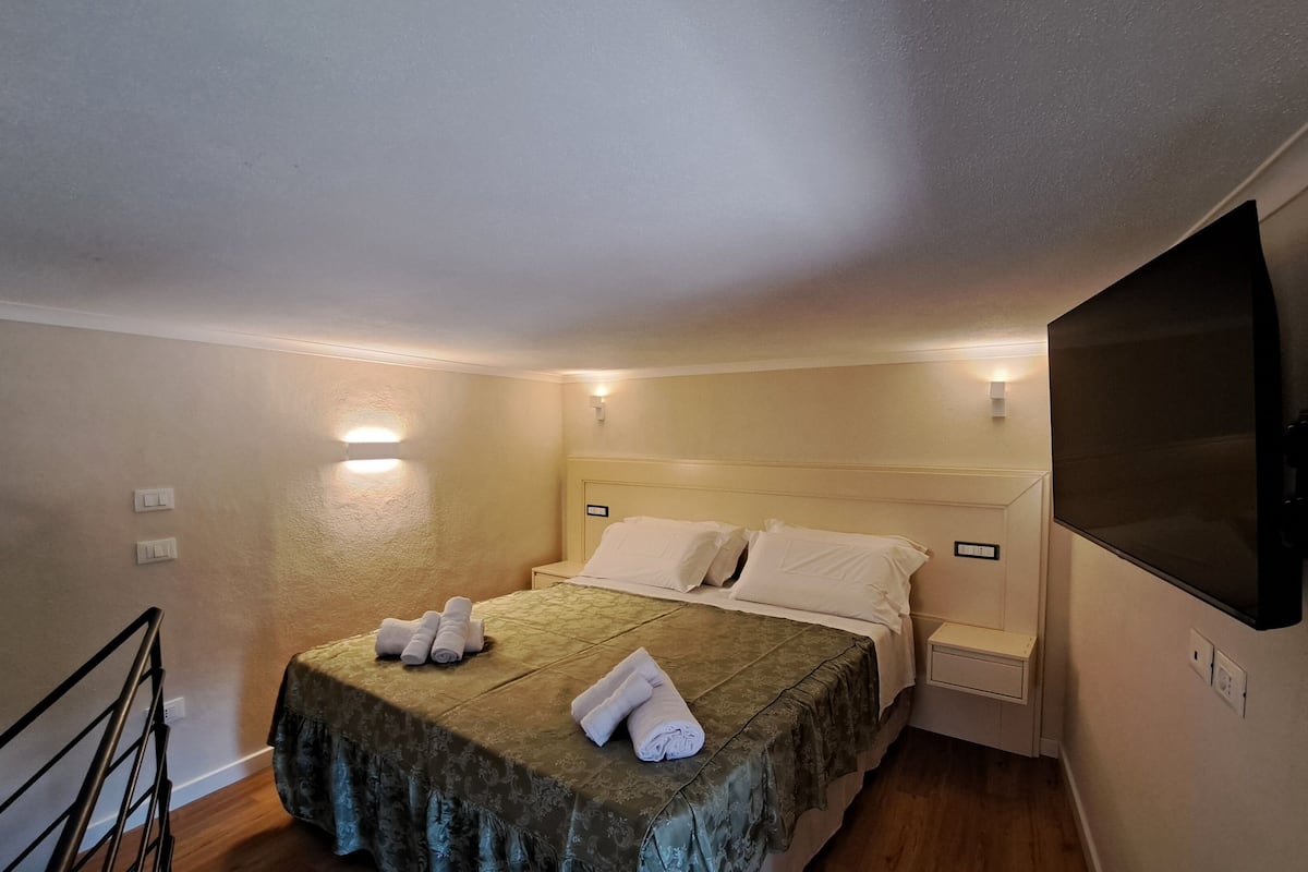 A hotel room with a bed, a TV mounted on the wall, and a small bedside table.