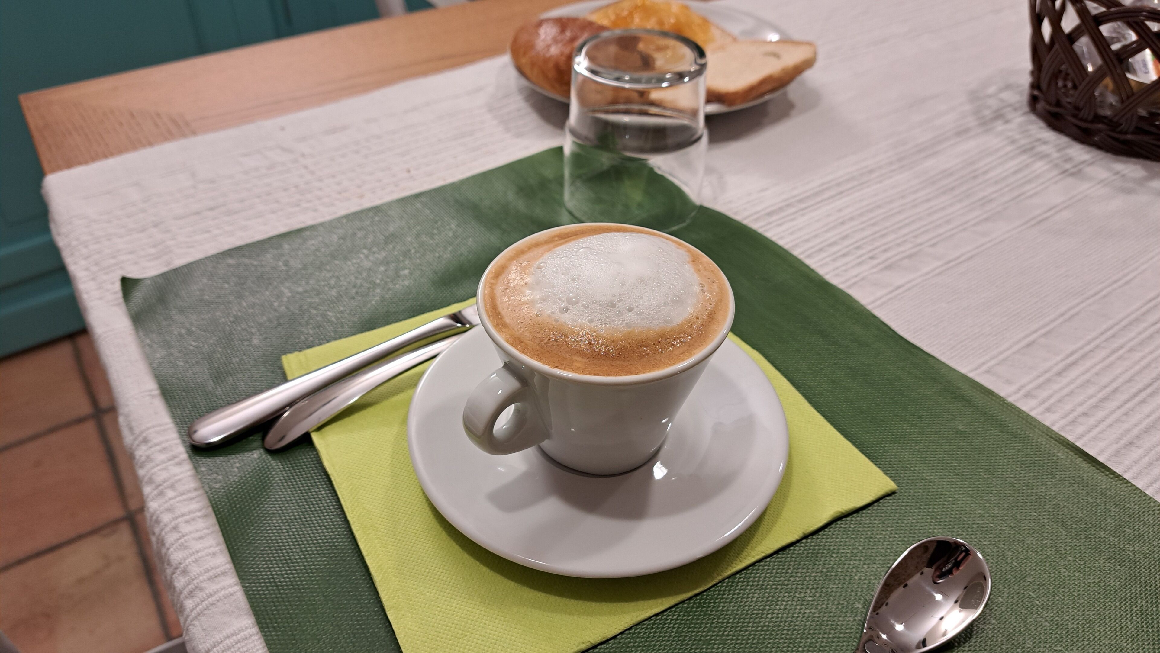 A cup of coffee on a white saucer with a spoon beside it, placed on a green placemat on a table.