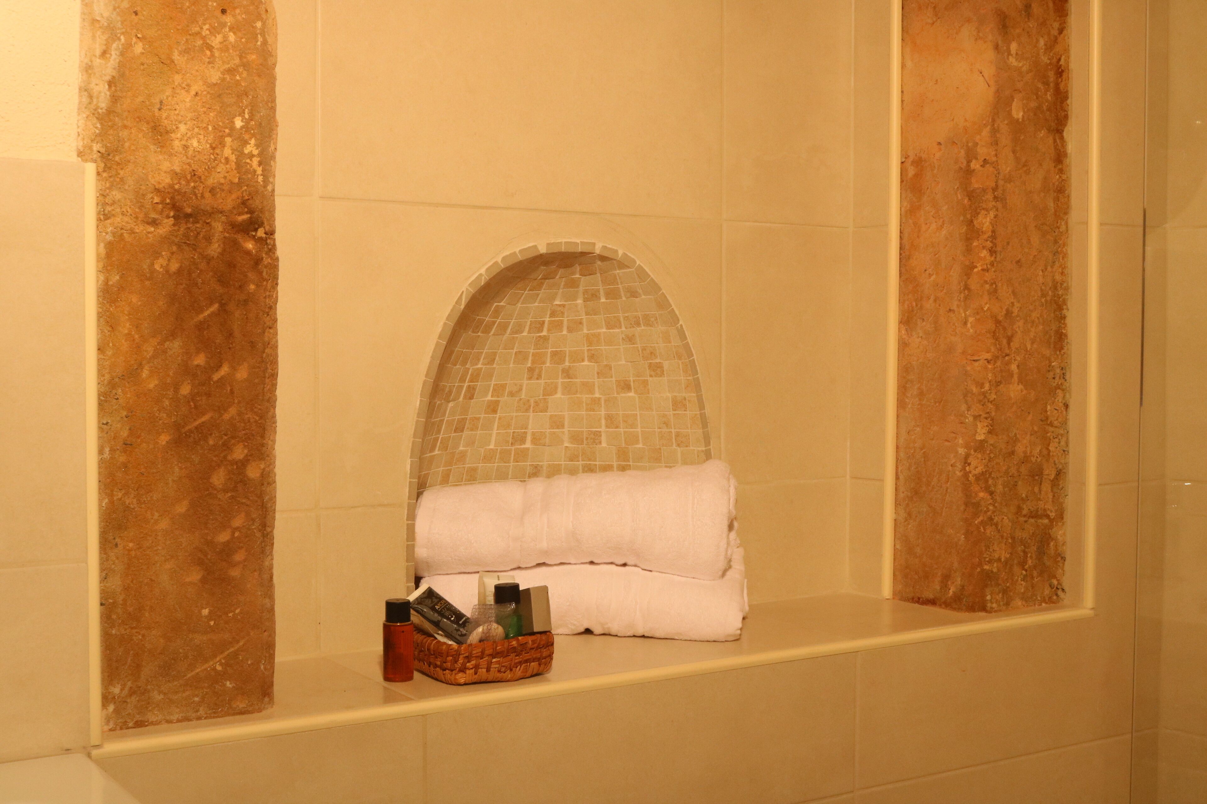 Un baño con pared de azulejos, un perchero y una cesta de artículos de aseo.