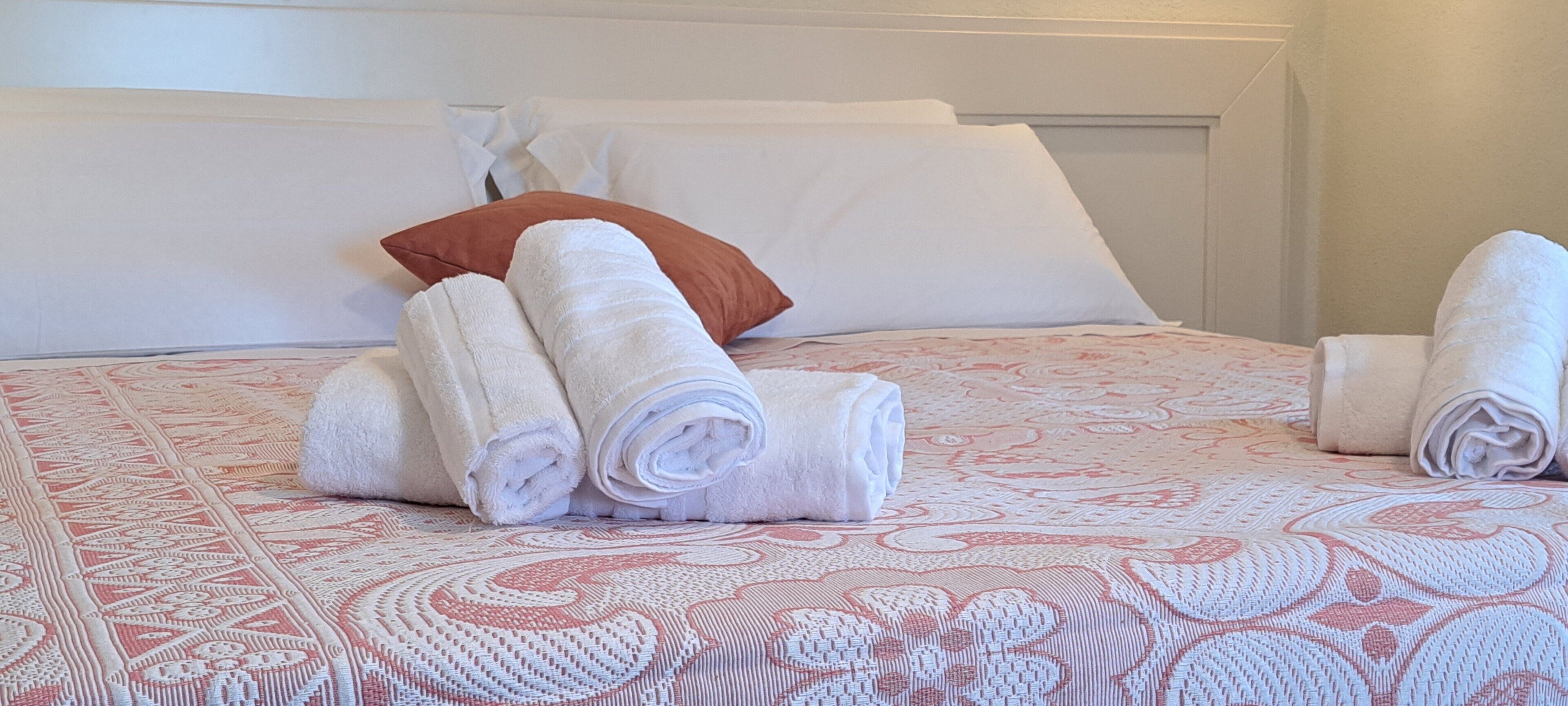 A neatly made bed with rolled white towels and a brown pillow.