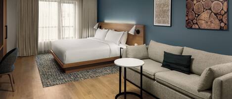 Una habitación de hotel con cama, sofá, una mesita y obras de arte en las paredes.
