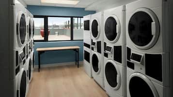 A laundry room with multiple washing machines, a bench, and a large window with a view of buildings.