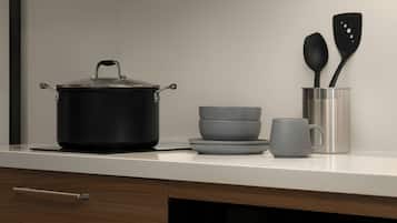 A kitchen counter with a black pot, a stack of gray bowls, a gray mug, and two black spatulas in a metal container.
