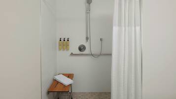 A shower area with a glass door, a towel on a chair, and toiletries on a shelf.