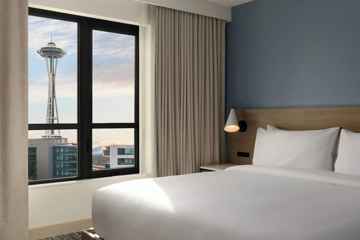 A hotel room with a large window, a view of a tower, a bed, and a nightstand.