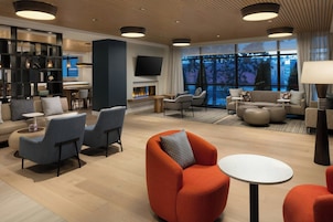 A modern hotel lobby with a fireplace, seating areas, and a large window offering a view of the outdoors.