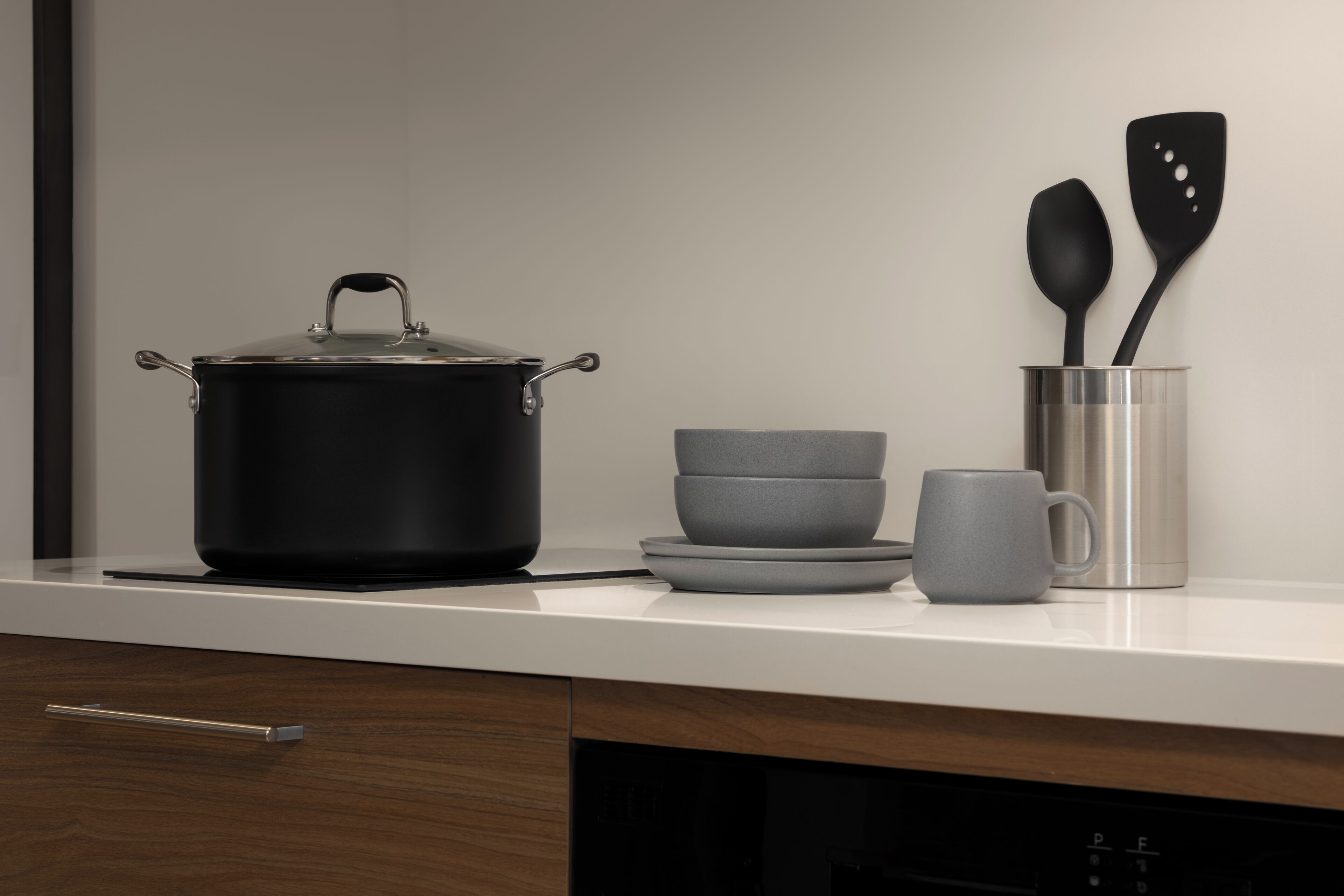 Een keukentafel met een zwarte pan, twee grijze kommen, een grijze mok en twee zwarte spatels in een metalen bak.