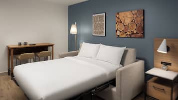 Quarto moderno com cama, escrivaninha, duas cadeiras, abajur e obras de arte na parede.
