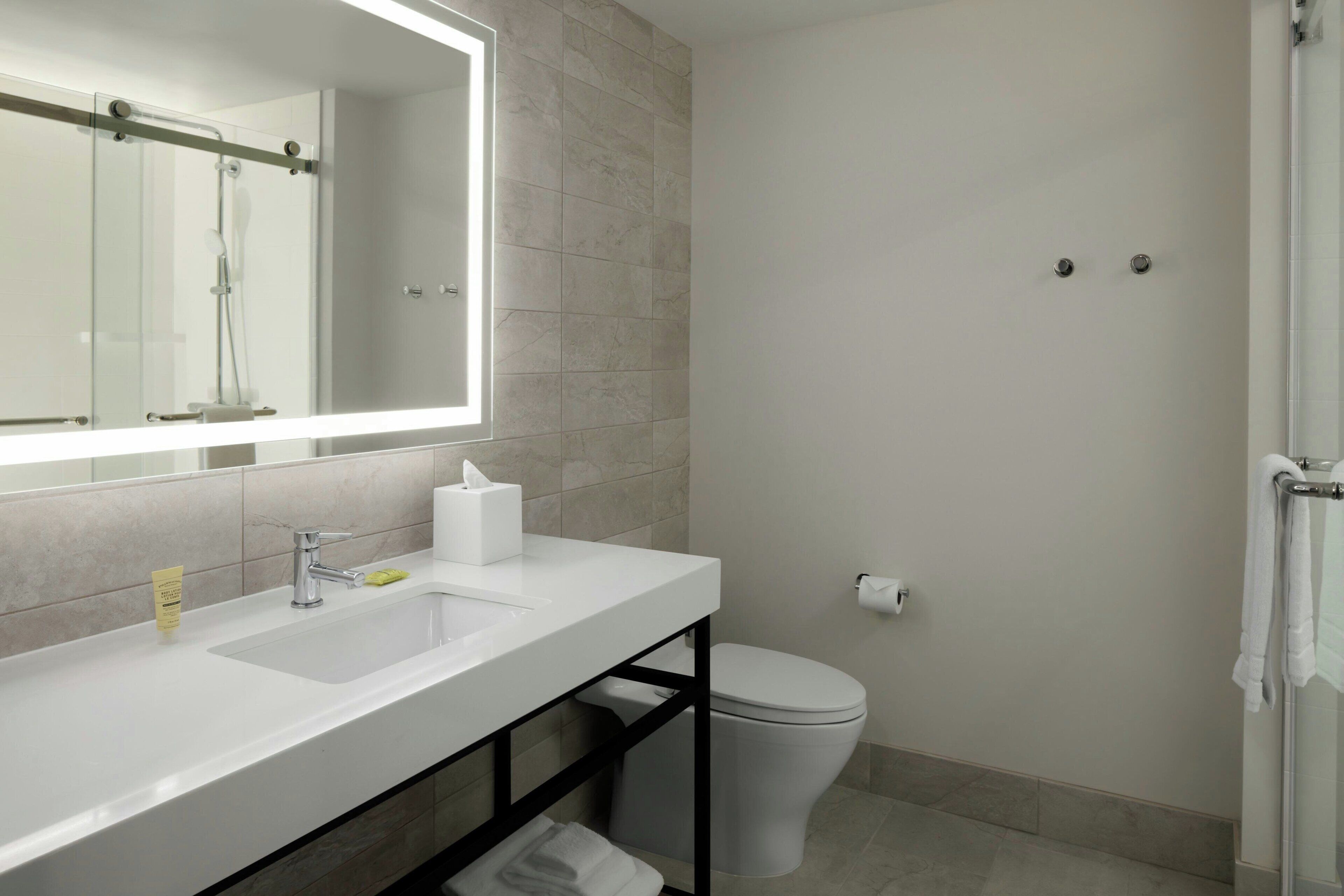 A modern bathroom with a large mirror, two sinks, a toilet, and a shower area.