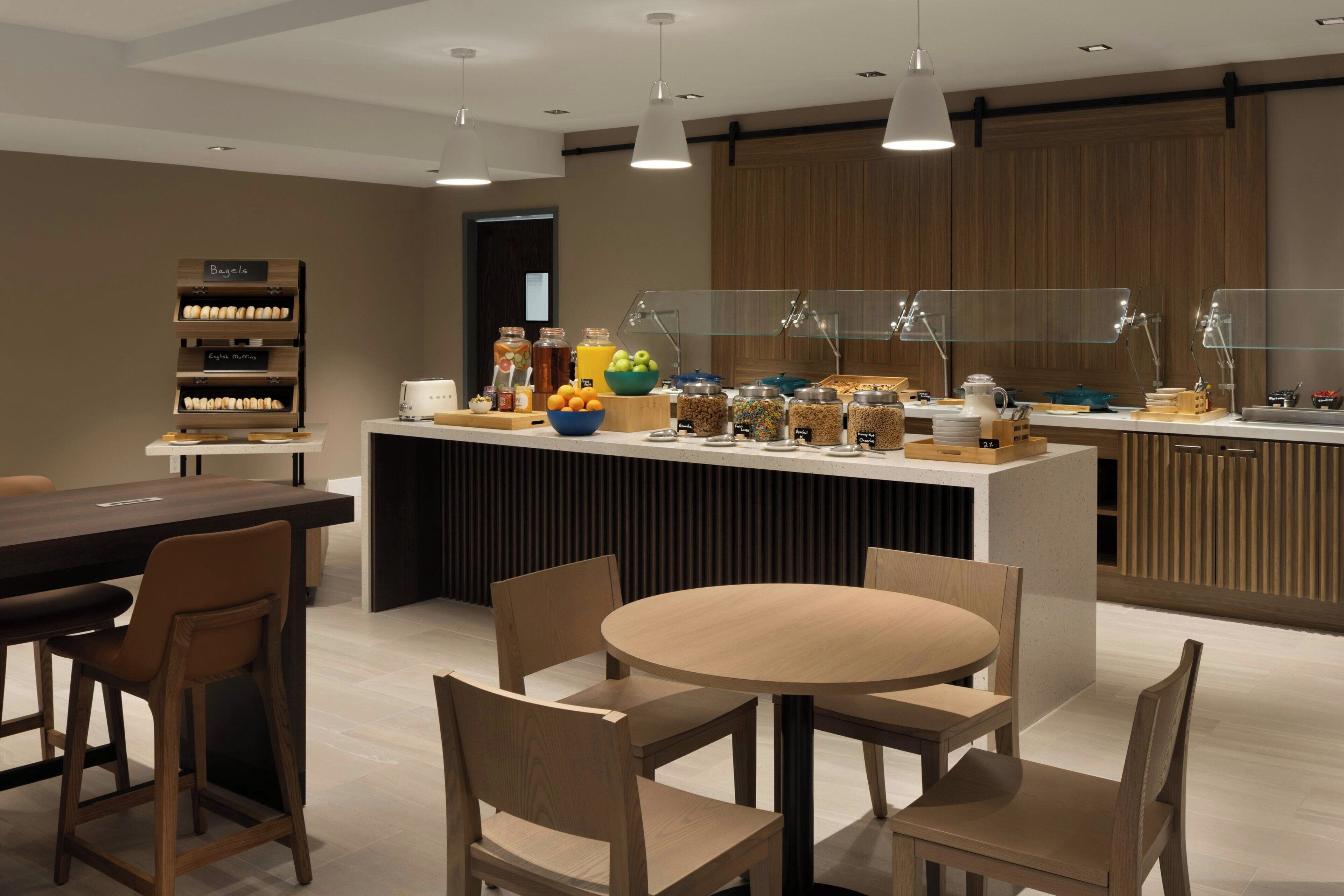 A modern breakfast area with a central island, seating, and a variety of food and drink options.