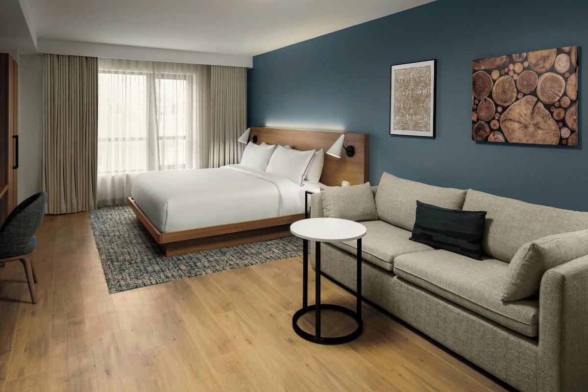 A hotel room with a bed, a sofa, a small table, and artwork on the walls.