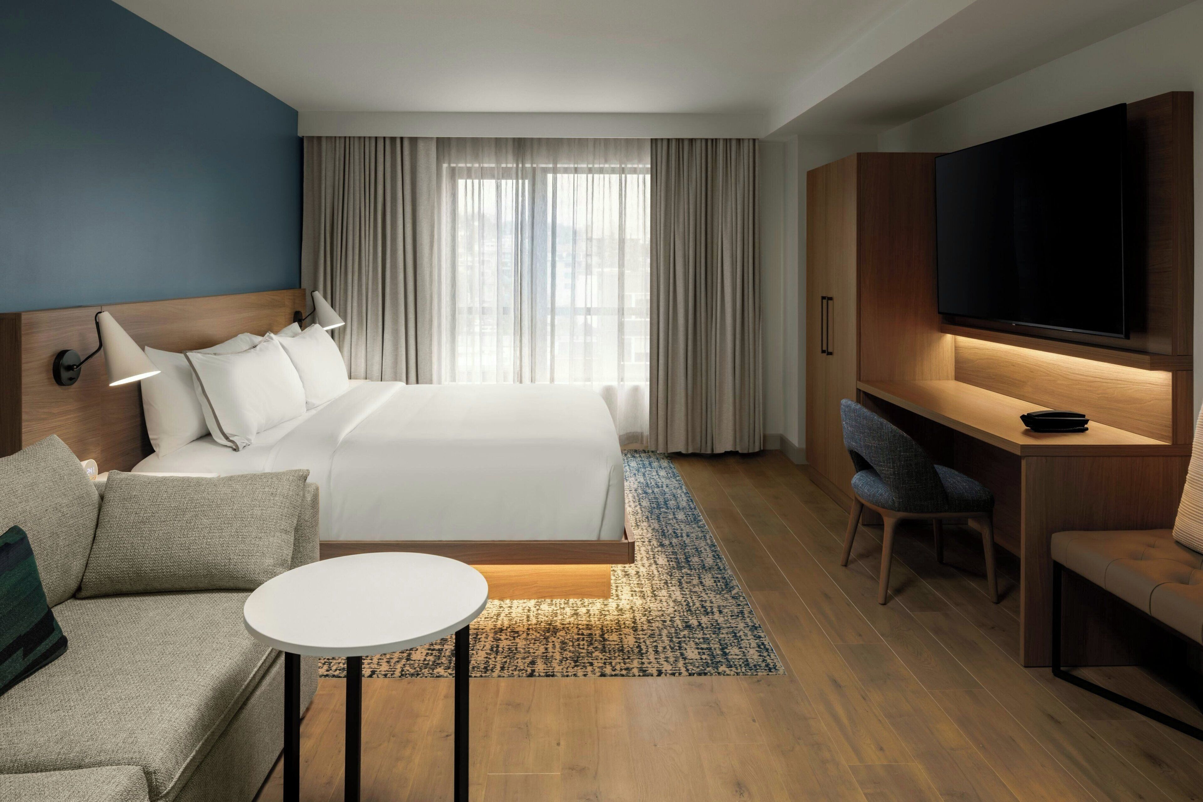 A hotel room with a bed, a desk, a TV, a sofa, and a small table.