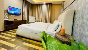 Une chambre d’hôtel moderne avec un grand lit, un téléviseur à écran plat, une table de chevet en bois et une plante en pot.
