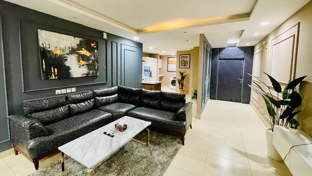Un salon moderne avec un canapé d’angle, une table basse et un grand tableau abstrait accroché au mur.