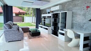 Un salon moderne avec un canapé gris, une table basse en verre, un bureau blanc et un téléviseur posé sur un meuble blanc.