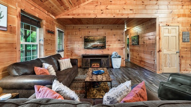 A log cabin interior with a fireplace, leather sofas, and a wooden ceiling.