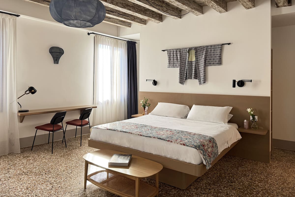 A bedroom with a bed, desk, chairs, and a hanging light fixture.