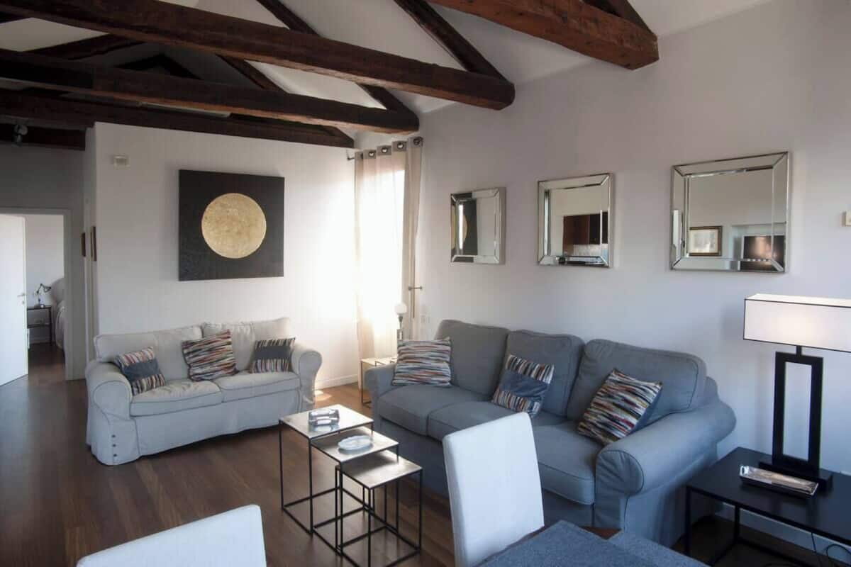 A living room with two sofas, a coffee table, and a lamp. There are three mirrors on the wall.