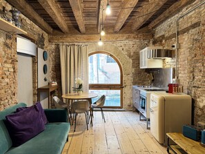 Eine rustikale Küche mit Holzbalkendecke, einem Essbereich mit Tisch und Stühlen, einem grünen Sofa und einem Fenster mit Ausblick.