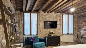 A rustic room with exposed brick walls, a wooden ceiling, a teal sofa, a bed, a TV, and a radiator. - PALAZZETTO SAN MARCO (Venice)