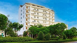 Ein mehrstöckiges Hotel mit heller Fassade, mehreren Balkonen und einem gepflegten Garten mit verschiedenen Bäumen und Sträuchern.