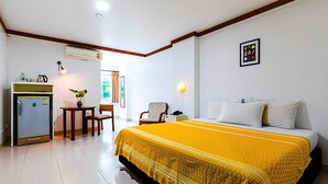 Habitación de hotel con cama, escritorio, silla, aire acondicionado y una mesita con un florero.