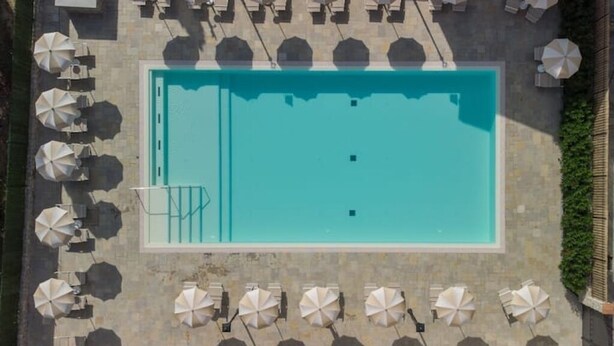 An aerial view of a rectangular swimming pool surrounded by multiple white umbrellas and lounge chairs, with a stone-tiled deck. - Limonaia 1 | Apartment Villa Carobbi (Firenze)