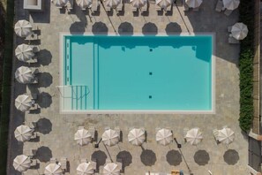 An aerial view of a rectangular swimming pool surrounded by multiple white umbrellas and lounge chairs, with a stone-tiled deck. - Limonaia 1 | Apartment Villa Carobbi (Firenze)