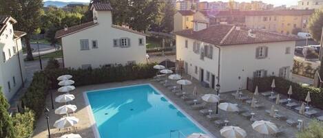 A swimming pool surrounded by lounge chairs and umbrellas, with buildings in the background.