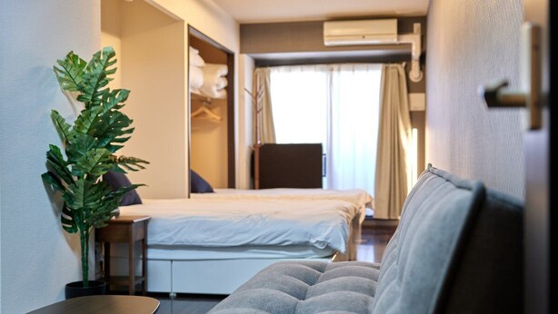 A compact hotel room with a bed, a sofa, a small table, and a potted plant. - XS15 XROSS STAY Namba7 (大阪市中央区島之内)