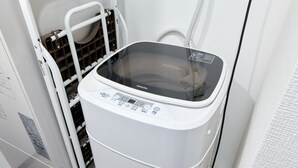 A compact, white, wall-mounted washing machine with a control panel and a transparent door, situated in a narrow hallway. - XS15 XROSS STAY Namba7 (大阪市中央区島之内)