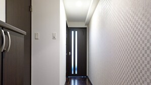 A narrow hallway with a dark wooden floor, a door with a metallic handle, and a wall with a checkered pattern. - XS15 XROSS STAY Namba7 (大阪市中央区島之内)