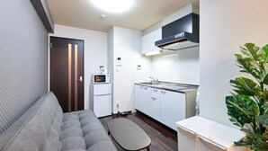 A compact living space with a sofa, a small table, a kitchenette with a microwave, and a plant. - XS15 XROSS STAY Namba7 (大阪市中央区島之内)