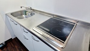 A kitchen with a stainless steel sink, a built-in stovetop, and white cabinetry. - XS15 XROSS STAY Namba7 (大阪市中央区島之内)