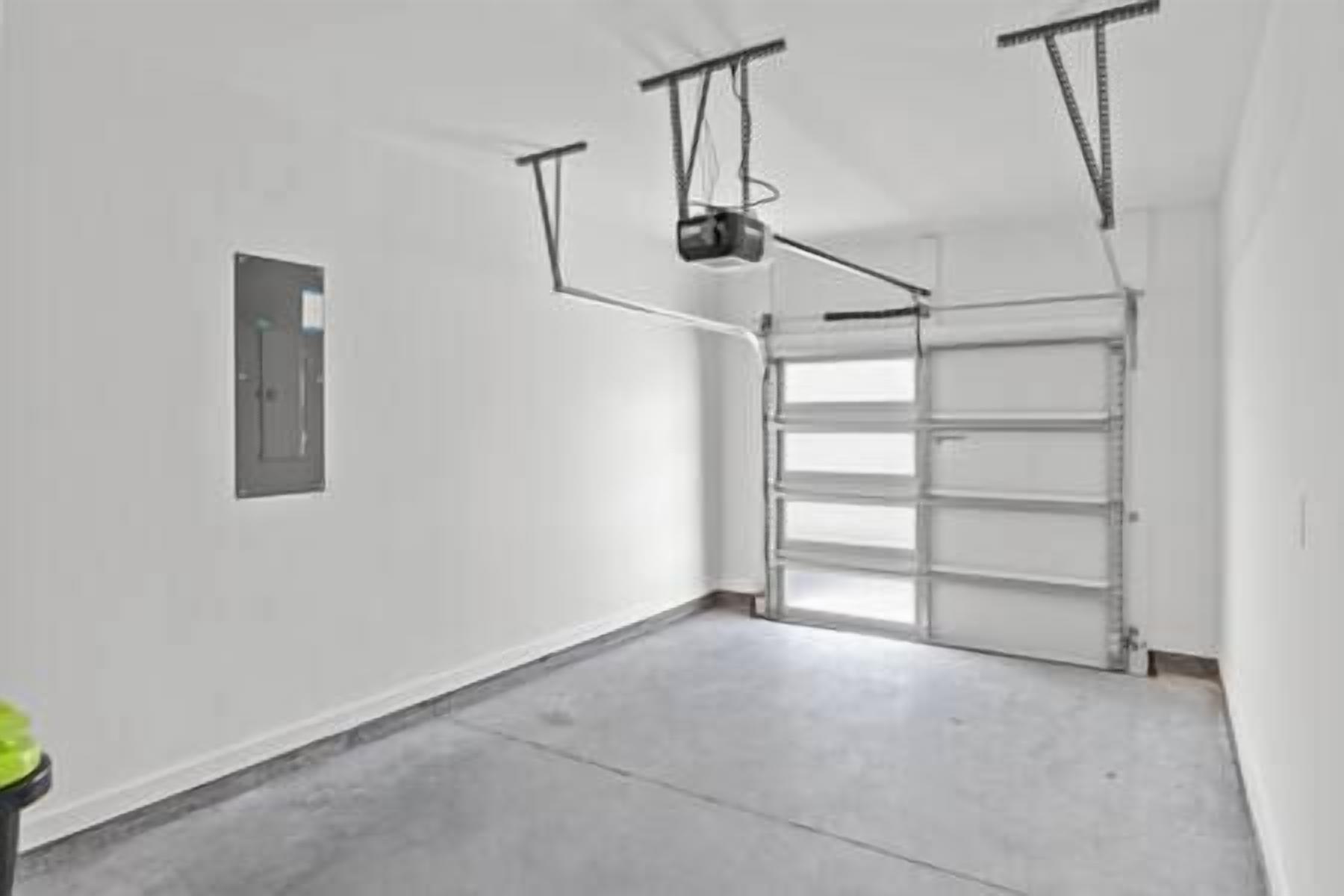 Een garage met een betonnen vloer, een witte deur en een projector die aan het plafond is bevestigd.