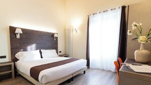 A hotel room with a large bed, bedside tables, a desk with a chair, a vase with flowers, and a window with curtains. - Limonaia 2 | Apartment Villa Carobbi (Firenze)