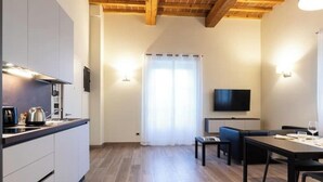 A modern kitchen with white cabinets and a wooden ceiling, a dining area with a table and chairs, and a TV mounted on the wall. - Limonaia 2 | Apartment Villa Carobbi (Firenze)