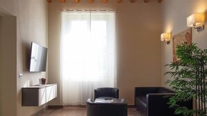 Un salon moderne avec un téléviseur à écran plat fixé au mur, un canapé noir, une petite table et une plante en pot.